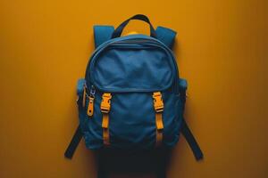 A vibrant blue backpack with yellow straps rests against a bright orange background, capturing a sense of adventure and exploration photo