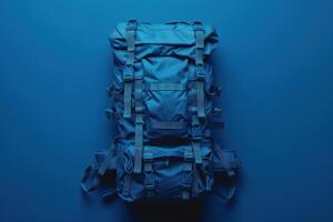 A vibrant blue backpack rests on a deep blue background, showcasing rugged straps and compartments, perfect for adventure or travel preparation photo