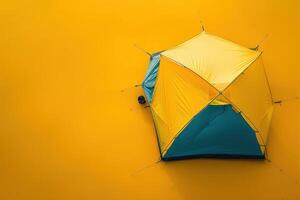 A vibrant yellow and blue camping tent set against a bright yellow backdrop in the golden light of late afternoon photo