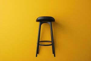 A sleek black stool stands against a vibrant yellow wall, showcasing modern design simplicity in a bright, inviting space photo