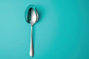 Shiny metal spoon resting on a vibrant turquoise background, reflecting light in a minimalistic still life composition photo