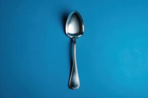 A shiny silver spoon rests gracefully on a vibrant blue background, glimmering in soft light, inviting thoughts of culinary delights and shared meals photo