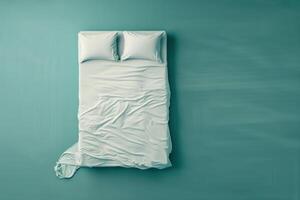 A serene, unmade bed with crumpled sheets and soft pillows against a calming teal backdrop in a cozy bedroom photo