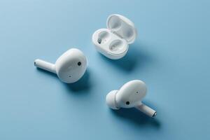 Stylish white wireless earbuds and their charging case arranged on a soft blue background photo