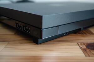 A close-up view of a sleek black gaming console resting on a wooden floor with visible USB ports, capturing modern technology in a cozy home environment photo