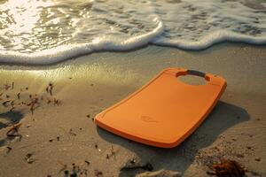 A vibrant orange surfboard resting on sunlit sand beside gentle waves at sunset on a tranquil beach photo