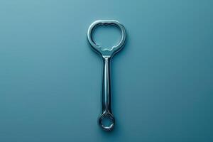 A shiny metal bottle opener resting against a smooth teal surface in soft lighting photo