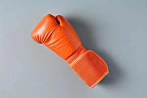 A striking orange boxing glove resting on a smooth gray surface, showcasing its vibrant color and intricate stitching details in morning light photo