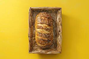 Freshly baked bread loaf with sesame seeds in a wicker basket on a bright yellow surface photo