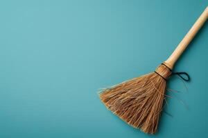 A rustic broom rests on a vibrant teal surface, ready for cleaning tasks with its natural bristles catching the light photo