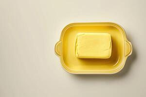 A creamy block of butter resting in a vibrant yellow dish on a light background, perfect for enhancing any culinary creation photo