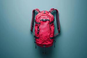 A vibrant red backpack hanging against a cool blue wall, showcasing its sleek design in a minimalistic indoor setting photo