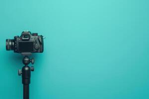 A black camera on a tripod against a vibrant turquoise background, ready for photography in a creative workspace photo