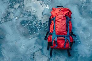 A vibrant red backpack resting on a textured, cool-toned surface, ready for adventure photo
