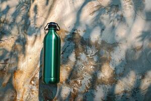 A green water bottle rests against a textured wall adorned with shifting shadows in soft afternoon light photo