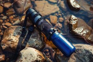 A striking blue water bottle rests perched on smooth stones by a tranquil stream during the golden hour of late afternoon photo