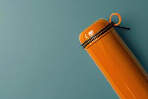 Bright orange container stands against a muted teal background, showcasing a minimalist design with rubber bands wrapped around its neck photo
