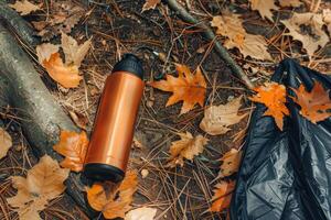 A copper water bottle rests on a bed of fallen autumn leaves in a serene forest setting photo