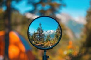 A tranquil campsite reflecting vibrant mountains and clear skies in a round mirror during a sunny day photo
