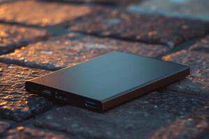 A portable charger rests on a cobblestone pathway at sunset photo