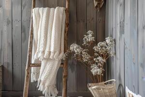 Cozy wool blanket draped on a wooden ladder beside dried flowers in a rustic interior setting photo