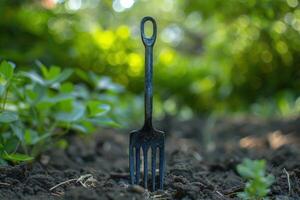 A garden fork stands upright in rich, dark soil surrounded by vibrant green plants on a sunny day photo
