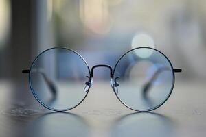 Close-up of stylish round glasses resting on a table with a blurred background during daytime photo