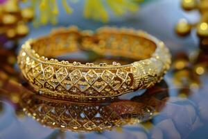 Intricately designed gold bangle with colorful accents displayed on a reflective surface photo