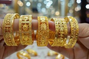 Hands showcasing a selection of intricate gold bangles at a market during the day photo