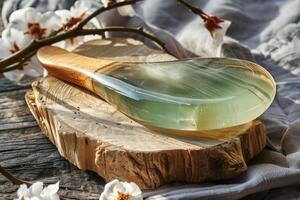 A bamboo-handled jade gua sha tool resting on a rustic wooden surface with blossoming branches nearby photo