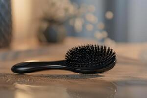 A black hairbrush resting on a wooden surface with a blurred background in a cozy indoor space photo