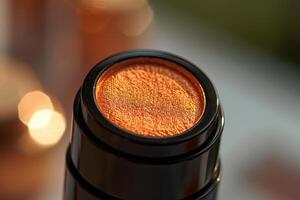 Close-up of a shimmering bronze highlighter in a black applicator against a blurred background photo