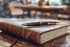 A leather bound journal rests on a wooden table beside a sleek pen in a cozy cafe photo