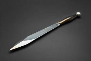A shiny, sharp dagger with a decorative handle placed on a dark surface photo