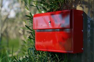 Bright red mailbox mounted on a fence surrounded by greenery in daylight photo