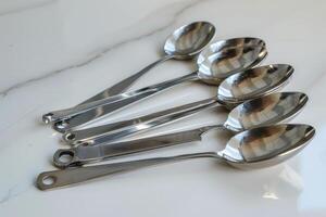 A collection of stainless steel teaspoons arranged on a marble surface with reflections photo
