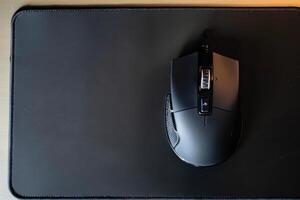 A wireless gaming mouse positioned on a black mouse pad in a well-lit workspace during the afternoon photo
