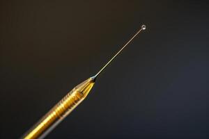 A close-up of a needle tip with a droplet of liquid poised at the end, illuminated against a dark background photo