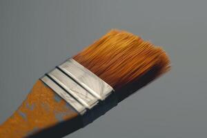 Close-up of a paintbrush with orange bristles resting against a gray background after a painting session photo