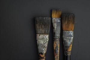 Three weathered paintbrushes on a dark surface highlighting tools used in artistic endeavors photo