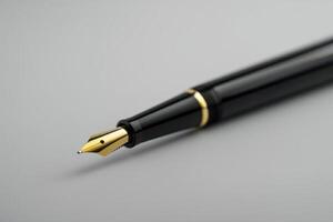 Close-up of a sleek black fountain pen with a golden nib on a gray background photo