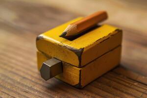 A close-up of a yellow pencil sharpener with a wooden pencil resting on top, placed on a rustic wooden table photo