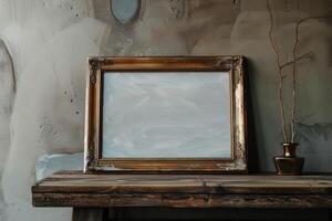 A vintage frame and simple brass vase on a rustic wooden table with a textured wall in a cozy interior setting photo