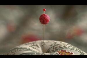 Close-up of a red sewing pin resting on a decorative pincushion in a softly blurred background photo