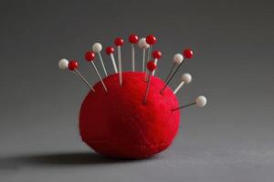 A vibrant red pincushion holds various colorful sewing pins against a neutral background photo