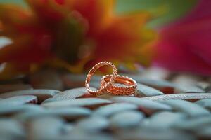 Beautiful rose gold rings resting on decorative stones with vibrant flowers in the background, captured in natural light photo