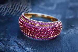 Elegant gold ring adorned with vibrant pink gemstones displayed on textured dark surface photo