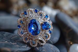 Elegant blue gemstone brooch displayed on smooth dark stones in a soft light setting photo