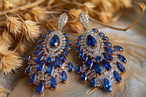 Elegant blue gemstone earrings displayed among dried grass on a soft fabric background photo