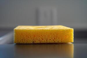 Yellow kitchen sponge resting on a countertop in a well-lit kitchen photo